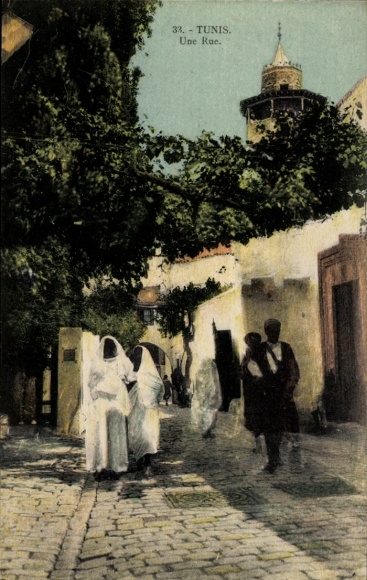 Postcard Tunis Tunisia, alley with people in traditional clothing, trees, tower in the background
