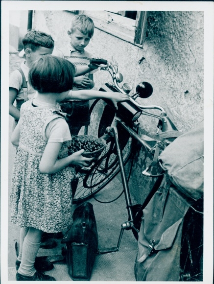 Photo Children look at the wall leaning bicycle, suitcase, basket with cherries